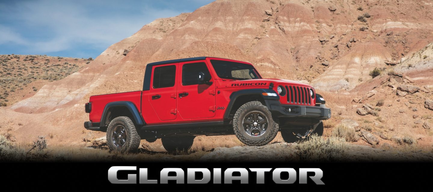 A 2023 Jeep Gladiator Rubicon towing two jet skis as it is driven along a beach near the water.