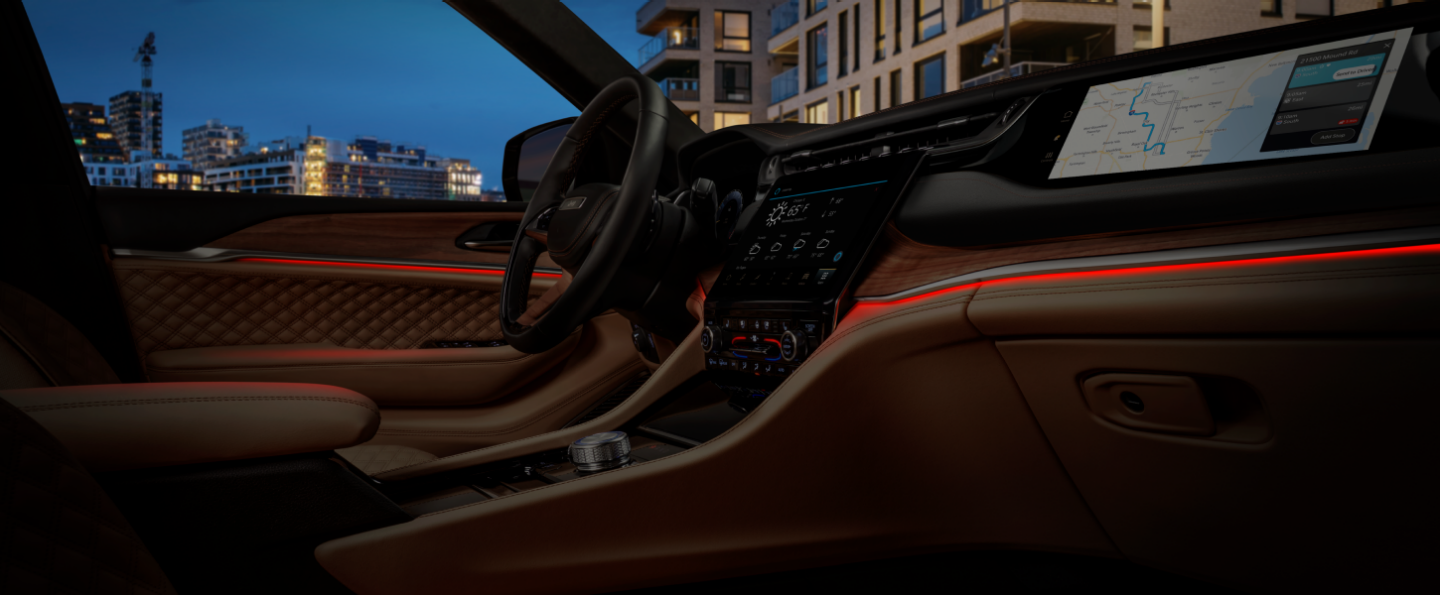 The front seat area of the 2024 Jeep Grand Cherokee Summit Reserve with red LED linear lighting woven through the door panels and dash.