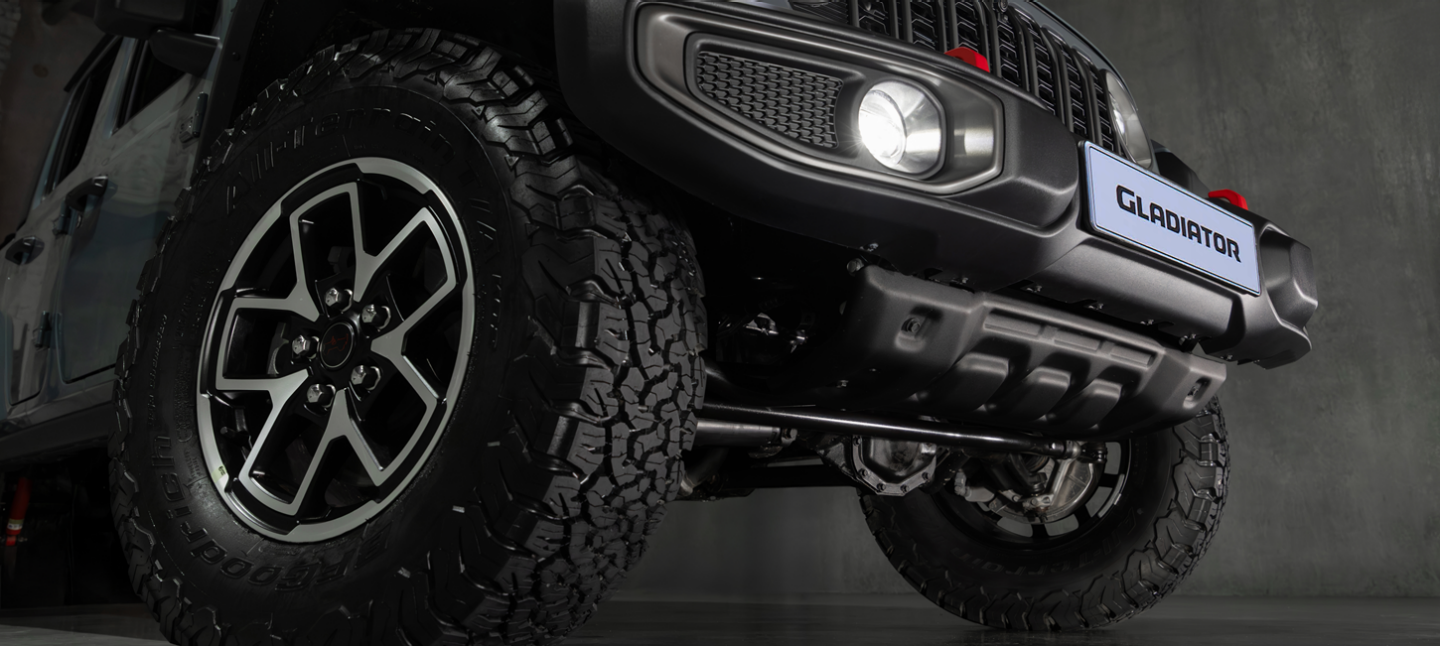 An olive green 2025 Jeep Gladiator Rubicon X travailing through deep snow off-road, in the mountains. Start Something New Sales Event logo.