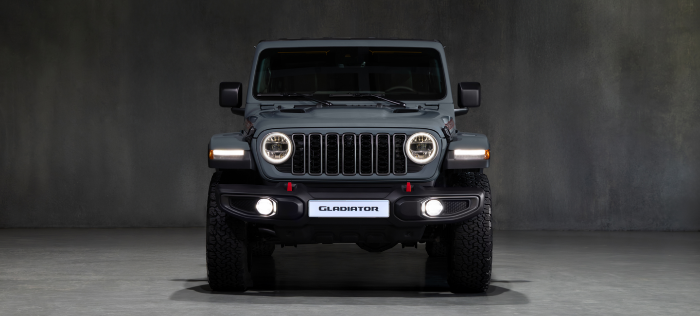 A blue 2025 Jeep Gladiator Mojave X with its doors and roof removed, ascending a trail in a hilly area off-road.