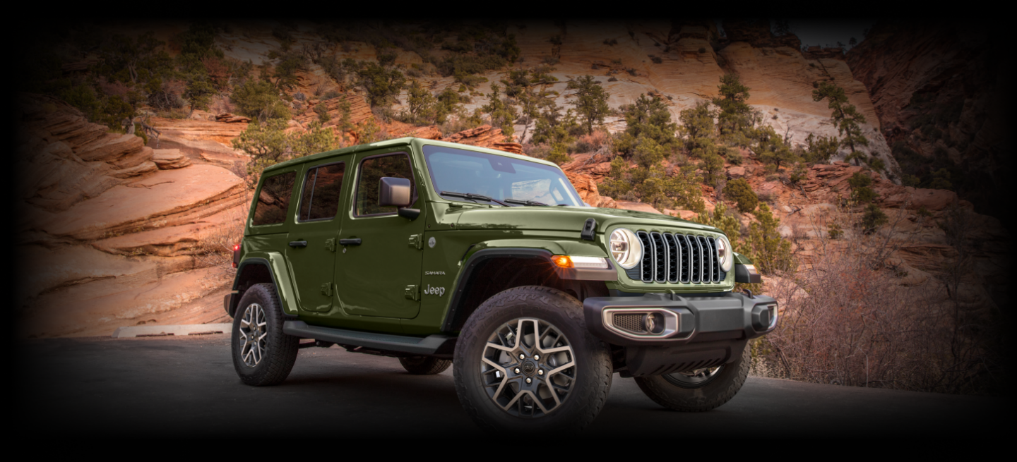 A angle from below of a green 2024 Jeep Wrangler Rubicon 4xe crawling over a stoney mound off-road.